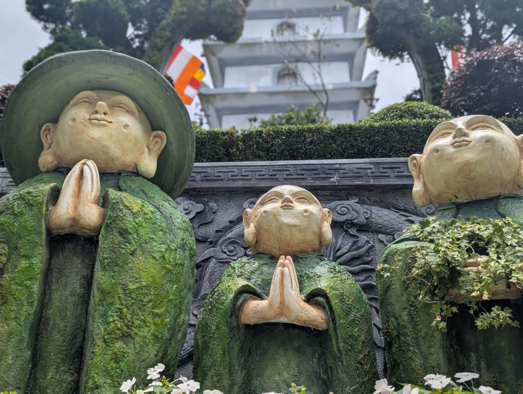 Gros plan sur trois statues de moines enfants en prière dans un jardin zen de Ba Na Hills.